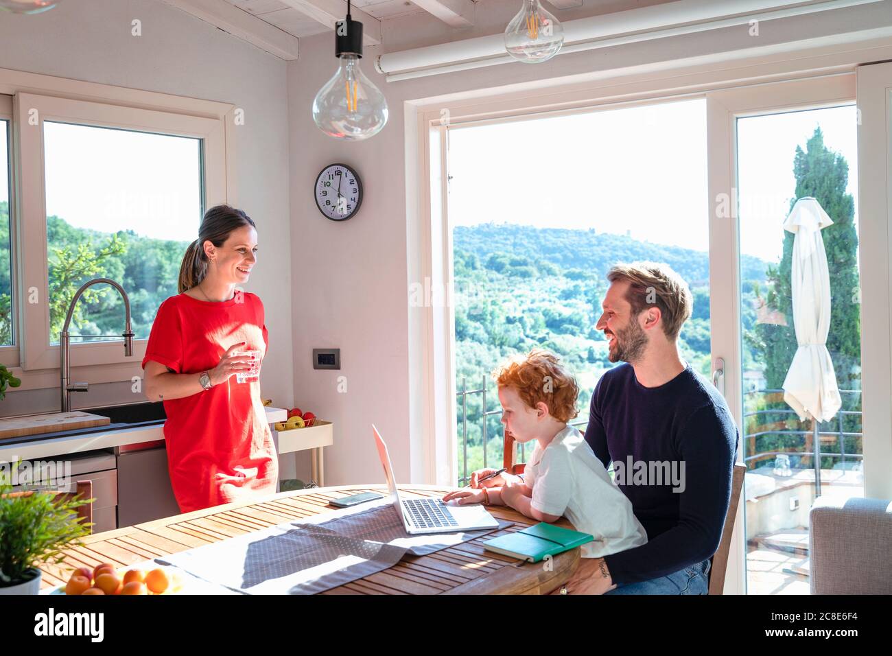 Smiling parents looking at each other while son using laptop in kitchen Stock Photo