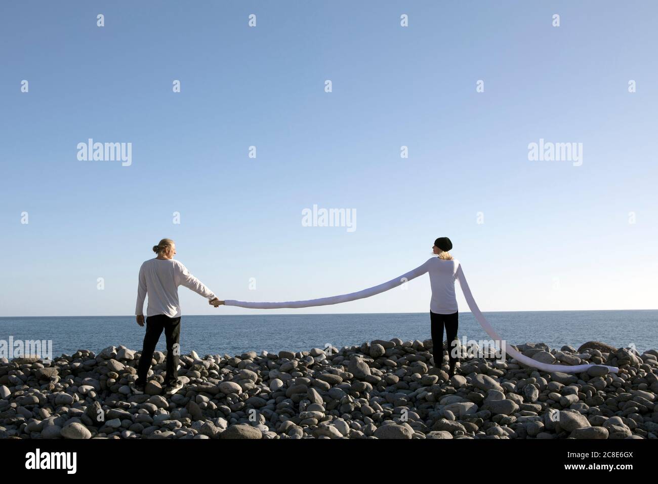 Woman with long arms holding man's hand at beach against clear sky Stock Photo