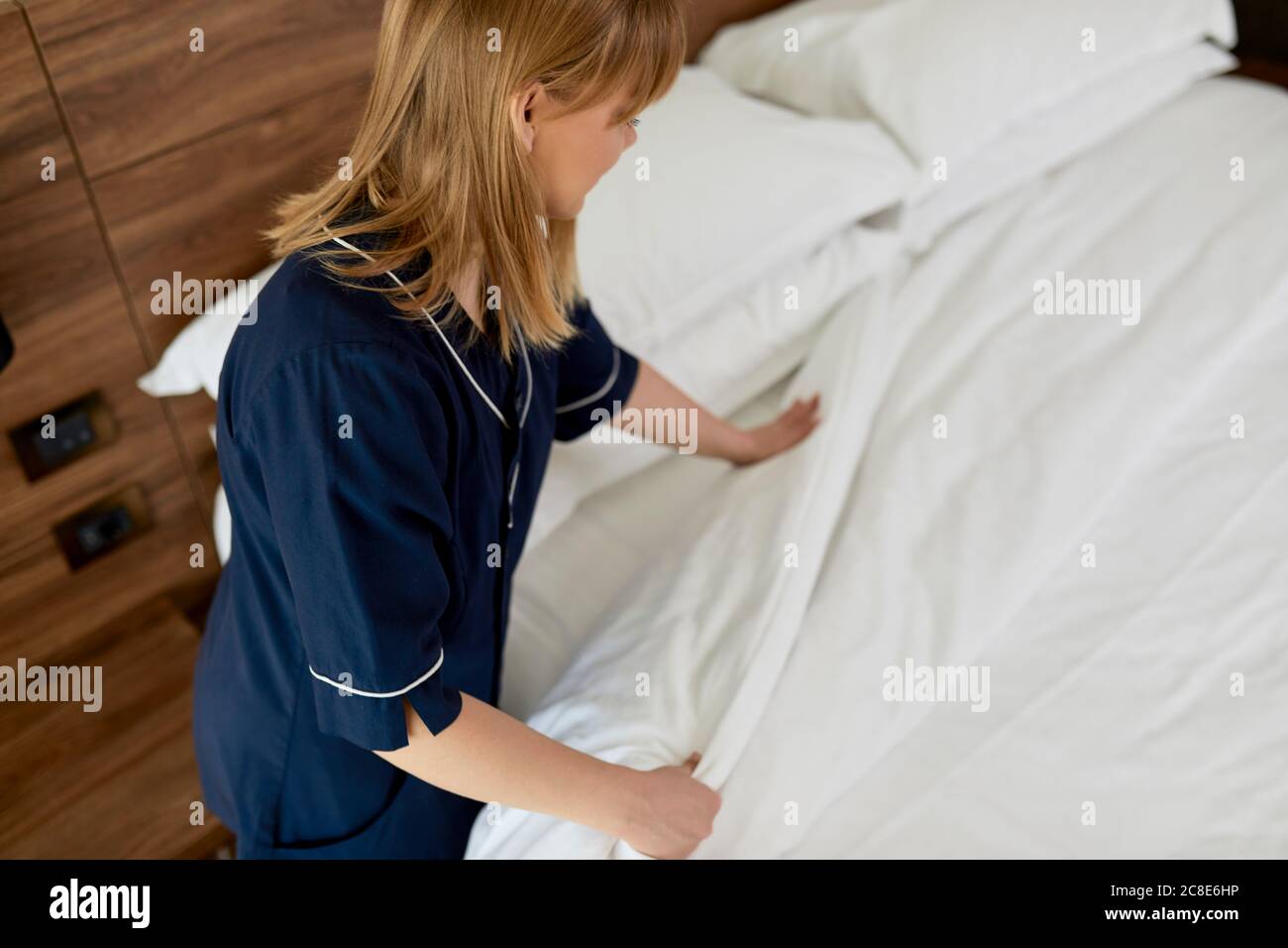 Maid arranging duvet on bed in hotel room Stock Photo