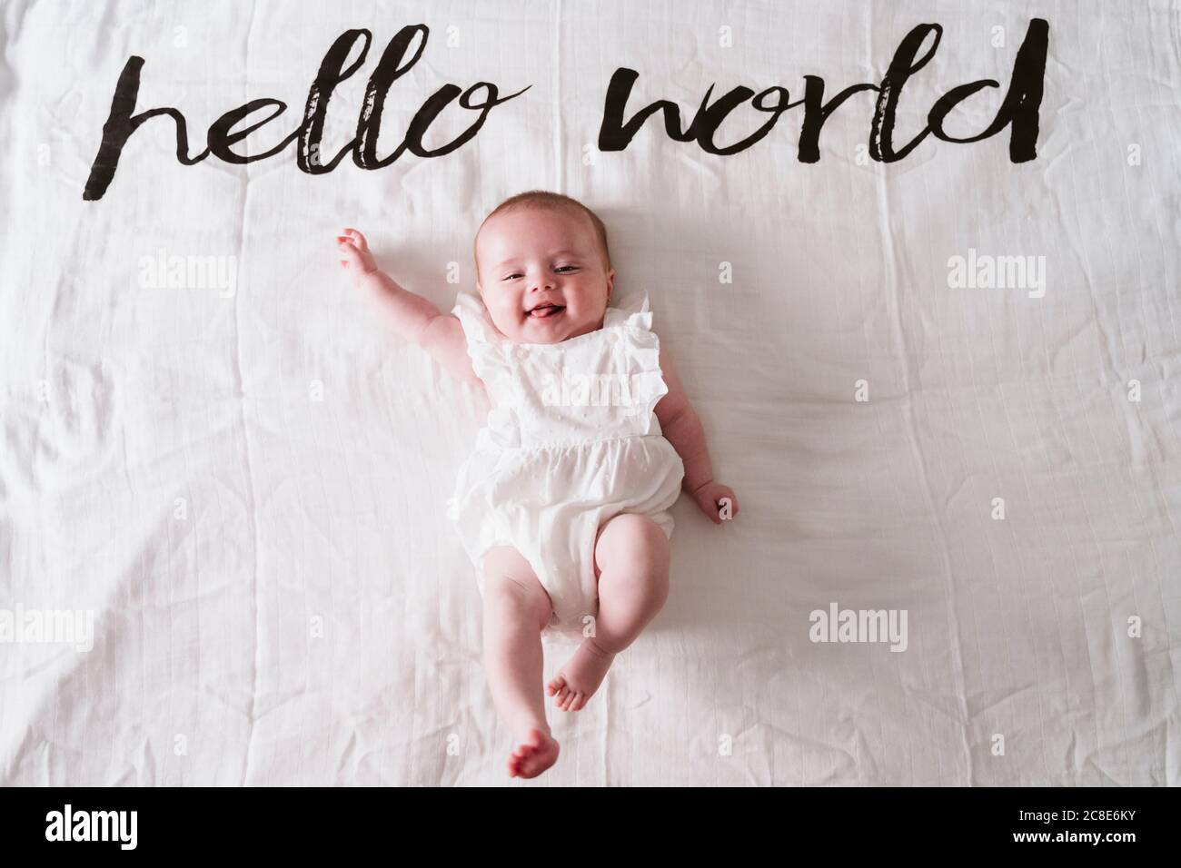 Happy cute baby girl lying on blanket under Hello World text at home Stock Photo