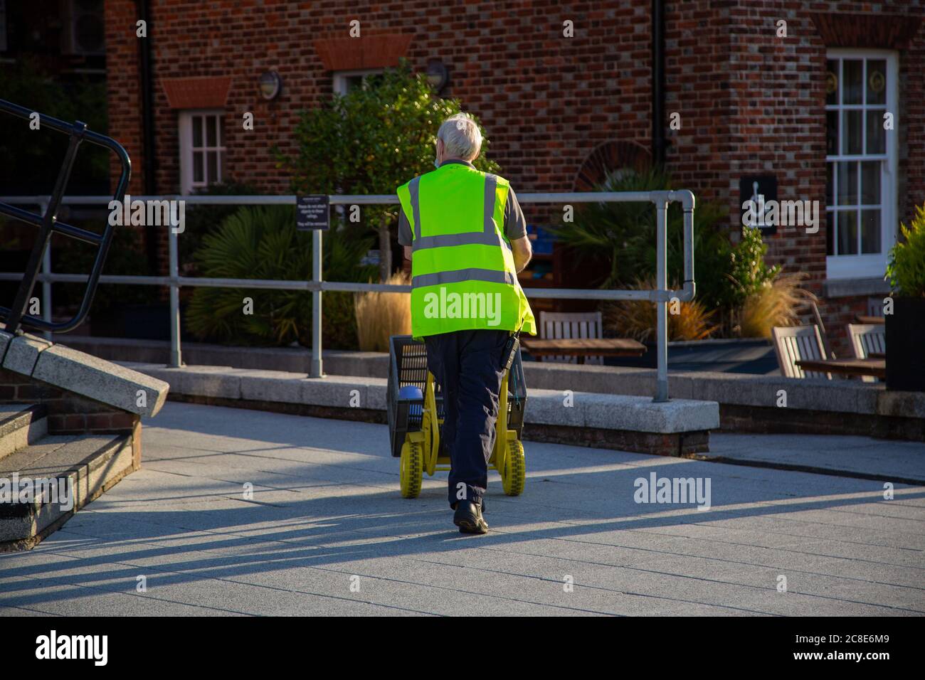 a worker in a hi-Vis or high visibility jacket pushing a sack truck in the street Stock Photo