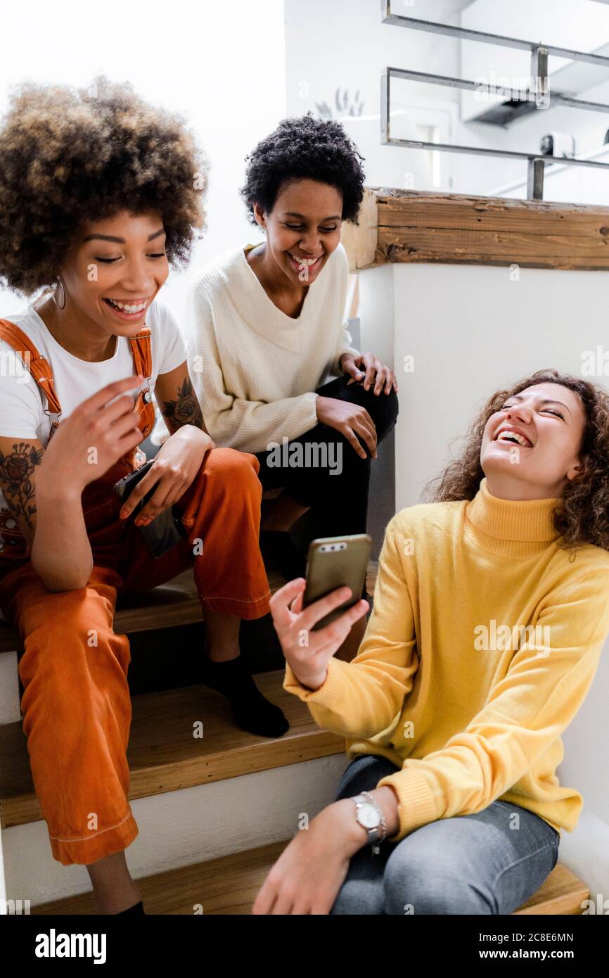 Three laughing young women having fun with smartphone at home Stock Photo