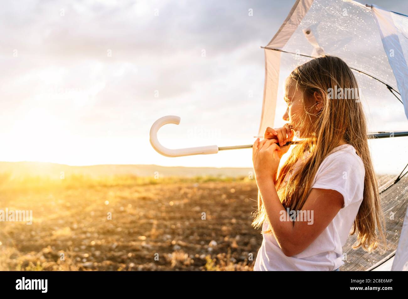 Girl with long blond hair holding umbrella while looking away during sunset Stock Photo