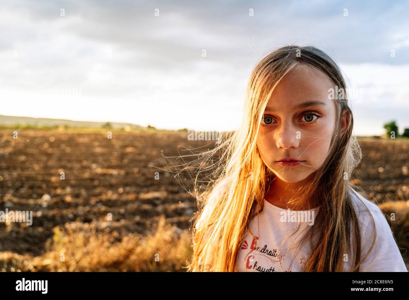 Pre-adolescent girl with long blond hair standing against sky during sunset Stock Photo