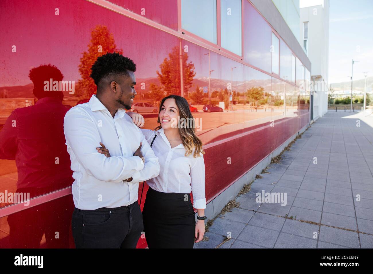 Multi ethnic colleagues talking while standing by red wall in city Stock Photo