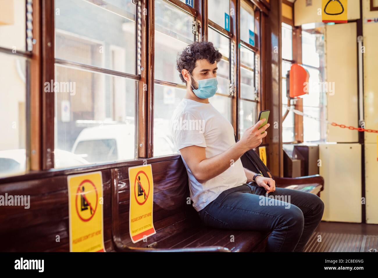 Young man wearing face mask using smart phone while sitting in tram Stock Photo