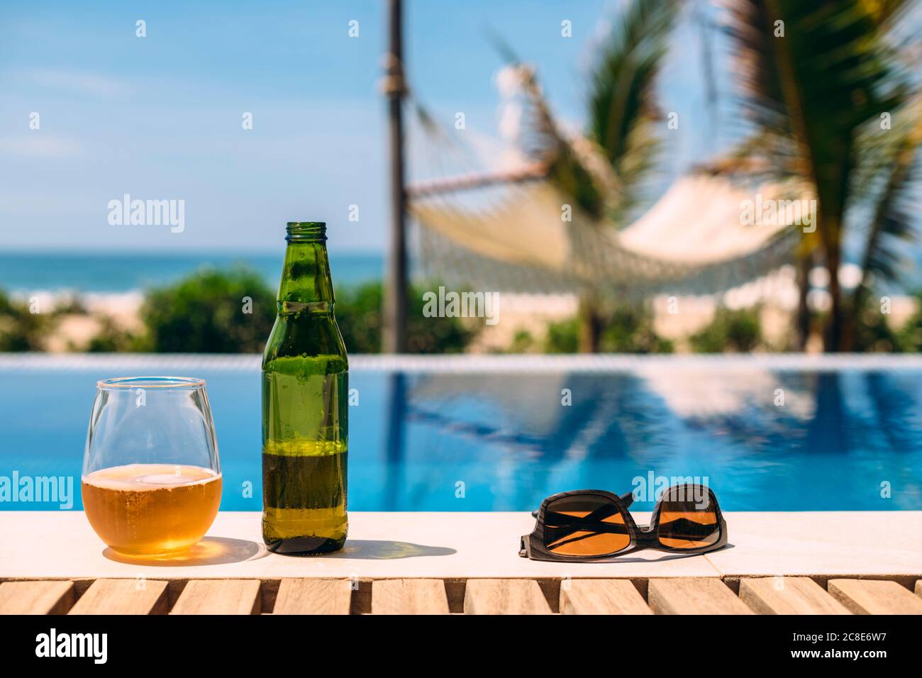 Sunglasses and open beer left at edge of outdoor swimming pool in summer Stock Photo