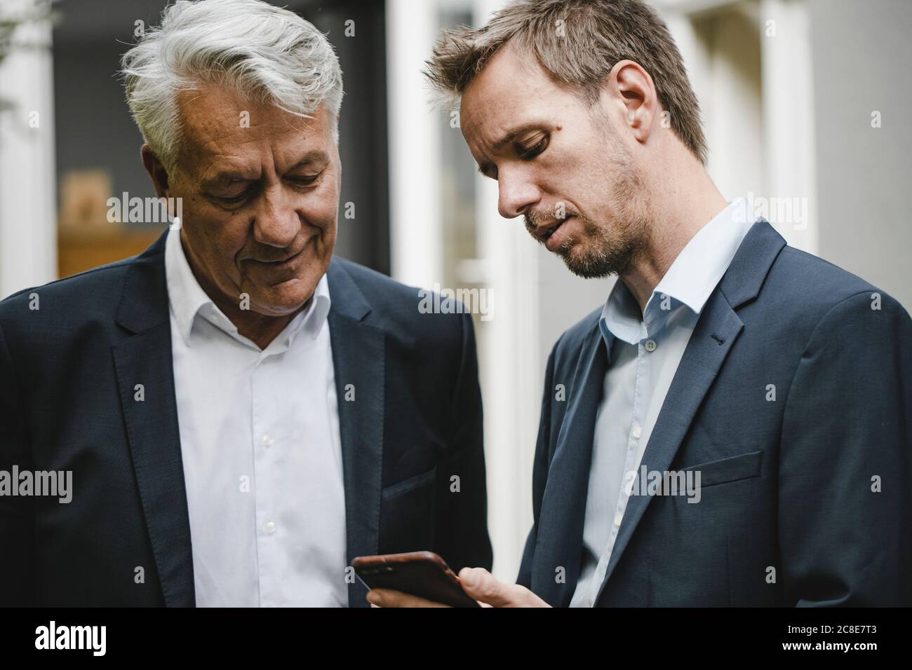 Two businessman standing in backyard, using smartphone Stock Photo