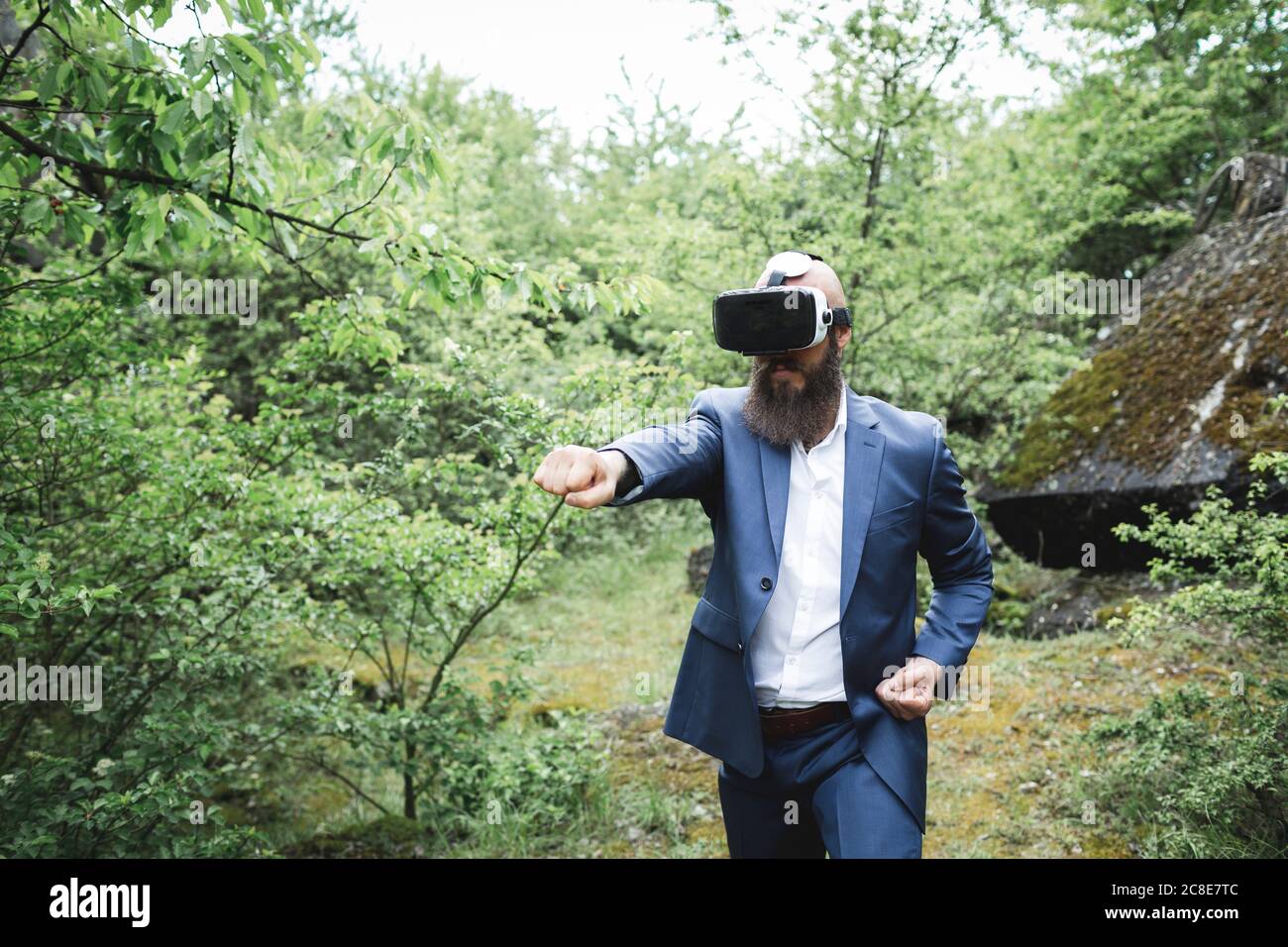 Businessman practicing martial arts while looking through virtual reality simulator against trees in forest Stock Photo
