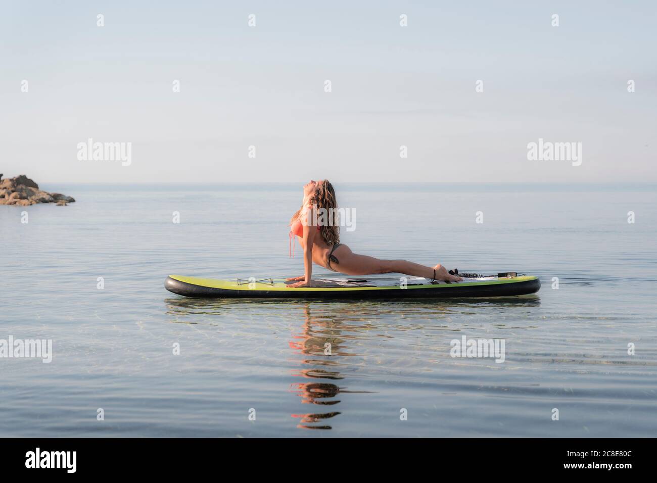 Woman practicing upward facing dog position on paddleboard over sea against sky Stock Photo