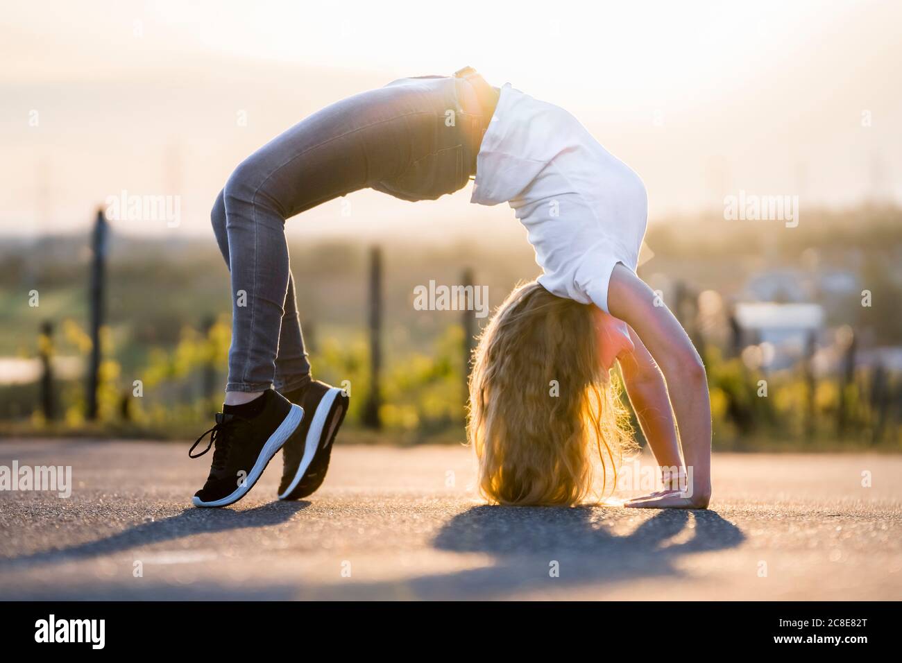 Young flexible woman doing backward bend on road during sunny day Stock Photo