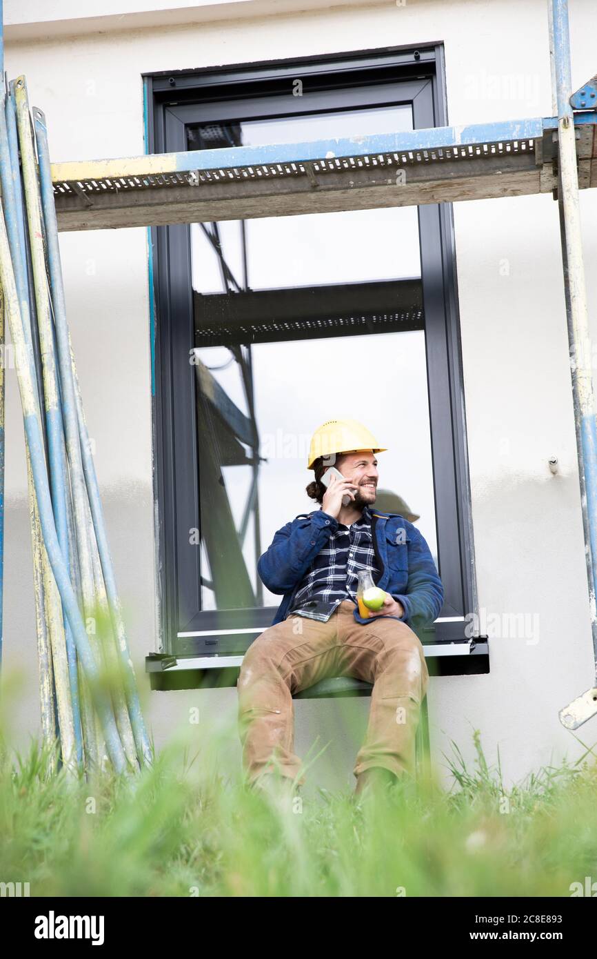 Construction worker talking over mobile phone while sitting against window Stock Photo