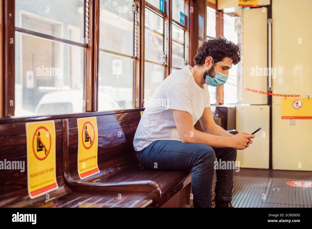 Man wearing face mask using mobile phone while sitting in tram Stock Photo