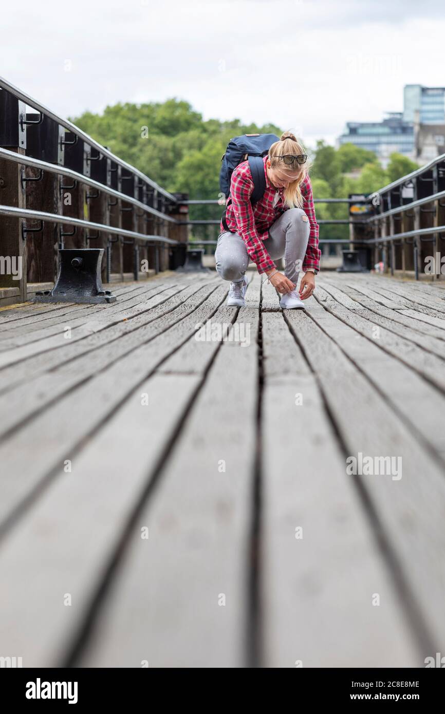 Mid adult woman tying shoelace while crouching on bridge in city Stock Photo
