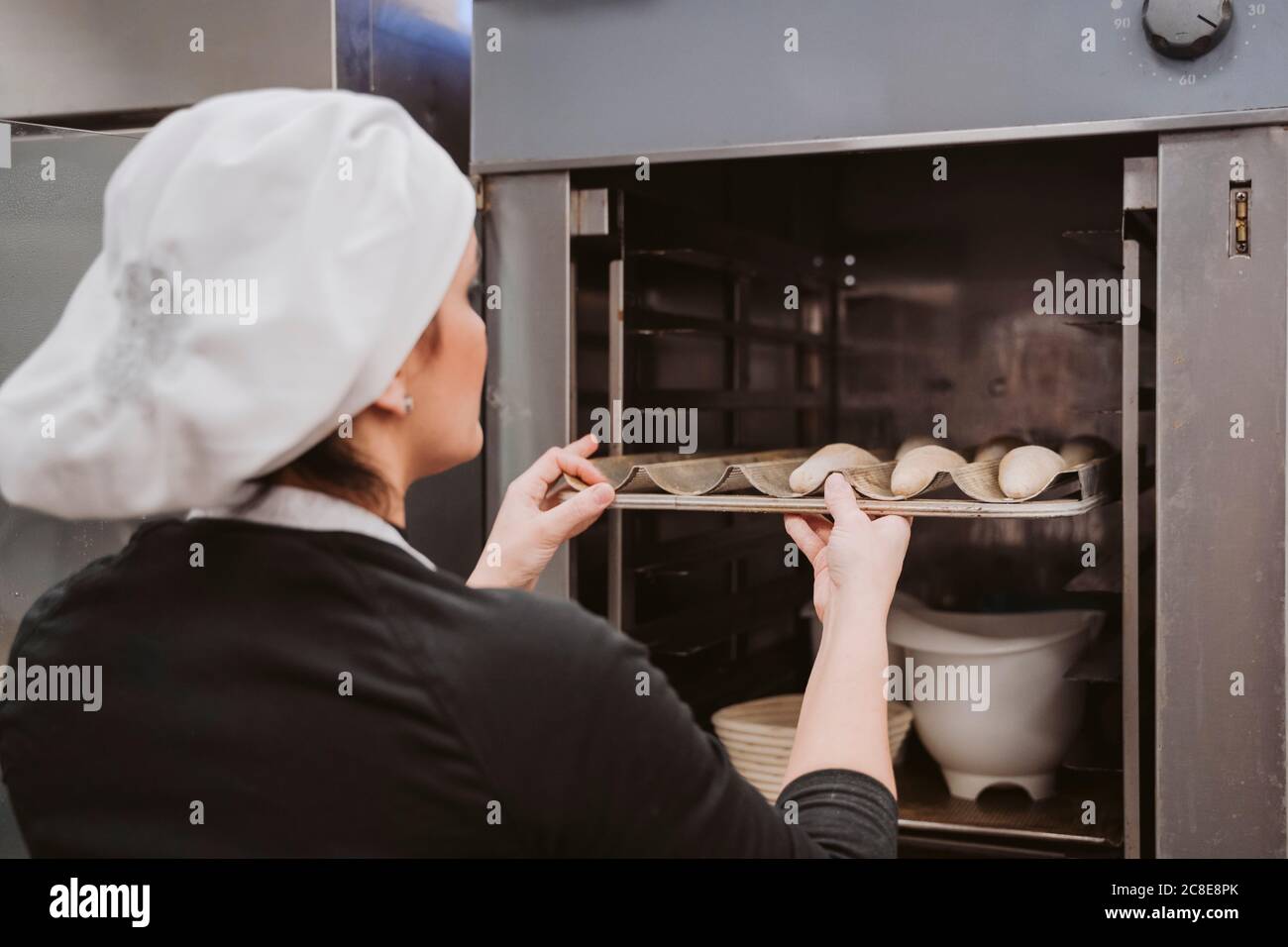 Female baker inserting baking pan in oven at bakery Stock Photo