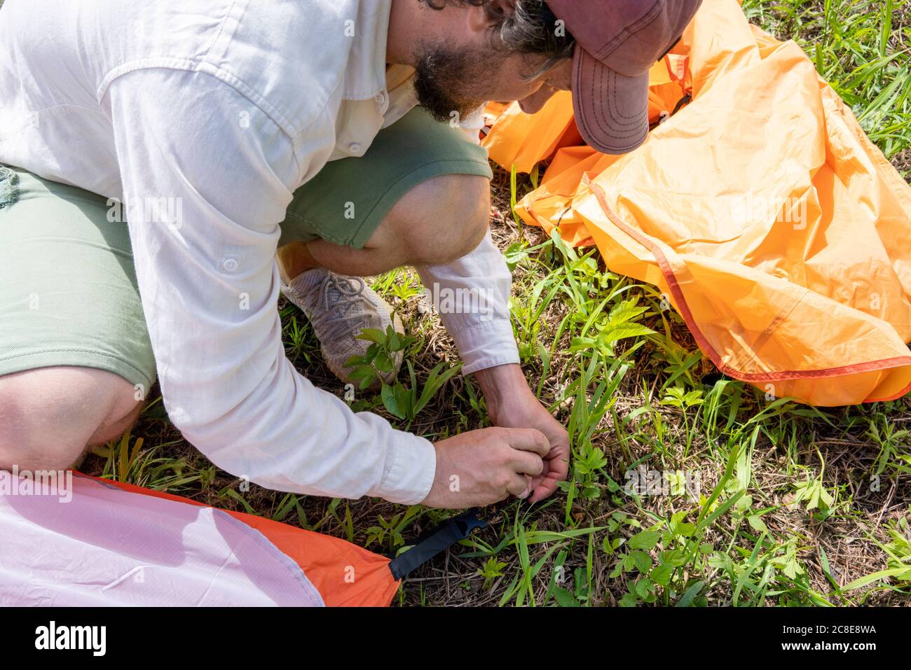 Mid adult man wearing cap installing tent on grassy land at campsite Stock Photo