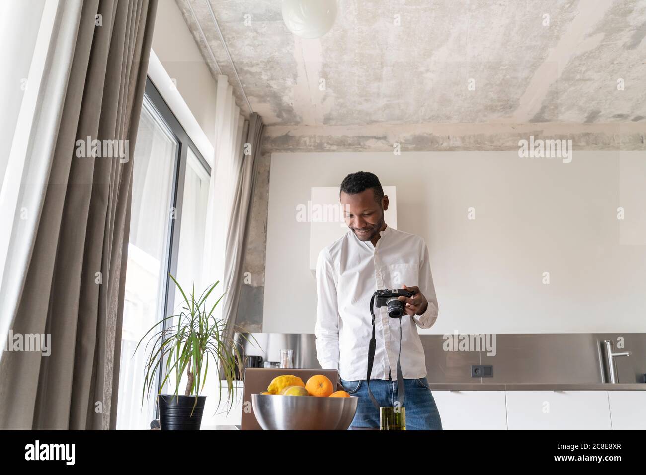 Smiling man using laptop and camera at home Stock Photo