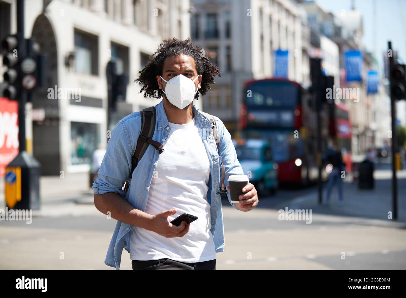 Portrait of young man wearing protective mask crossing the street ...