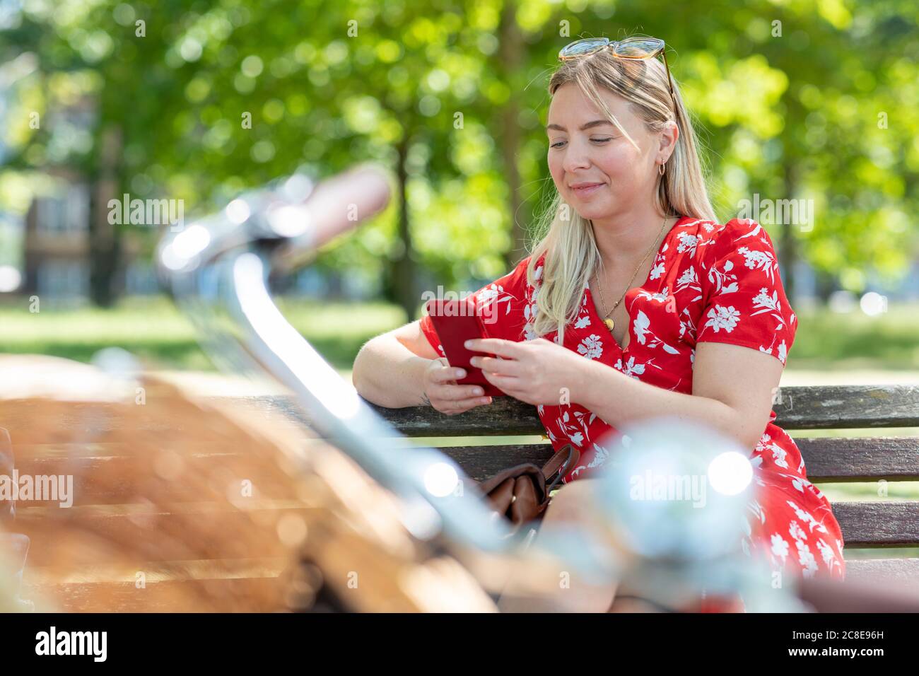 Beautiful woman using smart phone while sitting on park bench Stock Photo