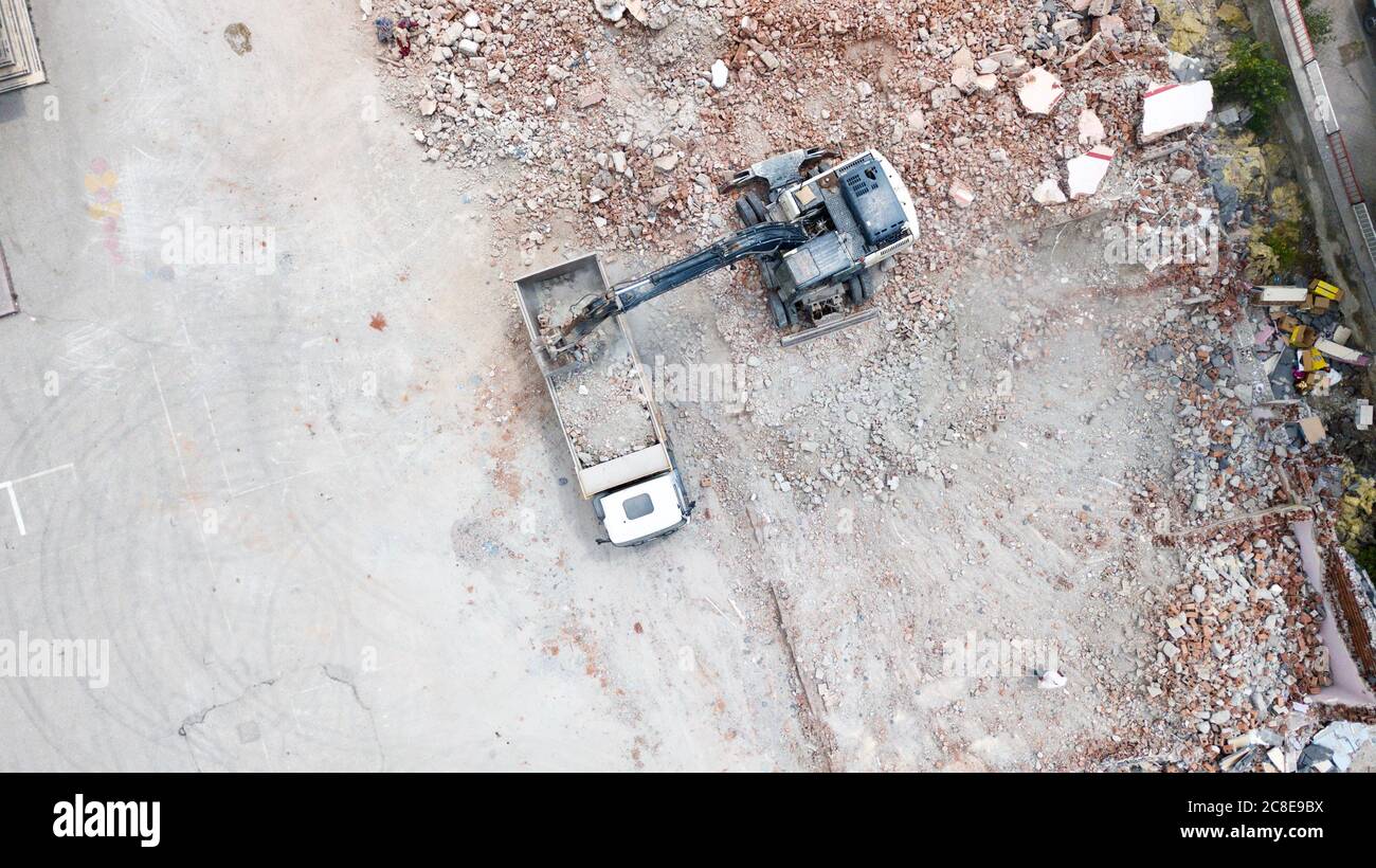 Aerial view of excavator demolishes an old building in city center. Destroyed concrete is loaded on the truck Stock Photo