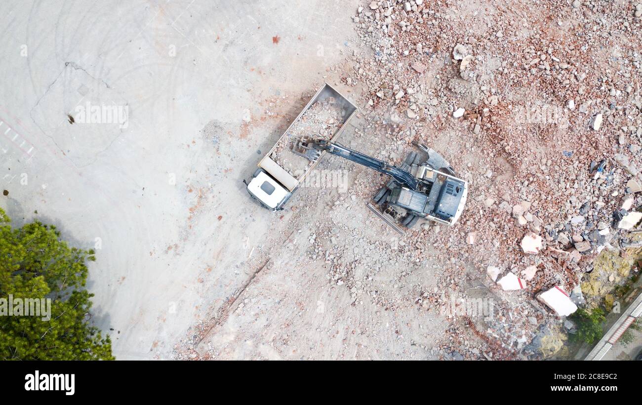 Aerial view of excavator demolishes an old building in city center. Destroyed concrete is loaded on the truck Stock Photo