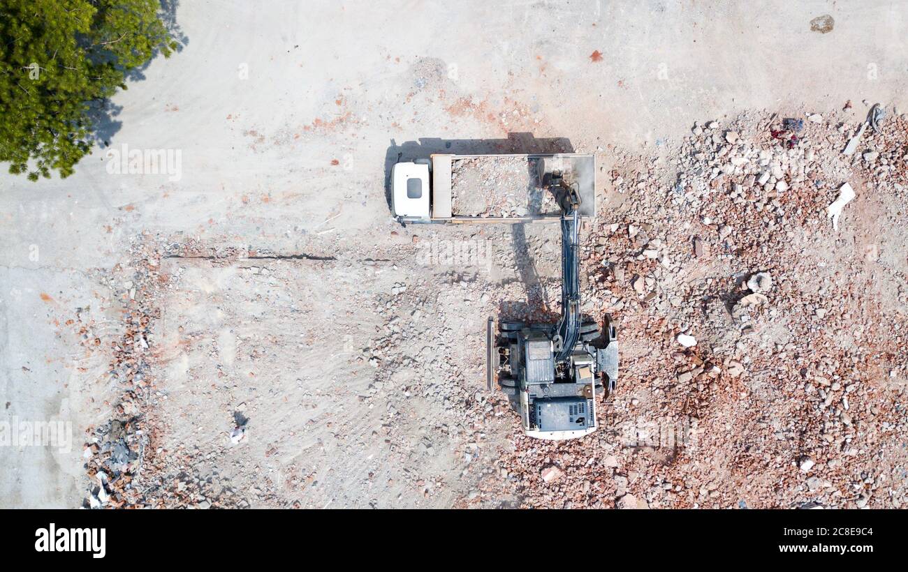 Aerial view of excavator demolishes an old building in city center. Destroyed concrete is loaded on the truck Stock Photo