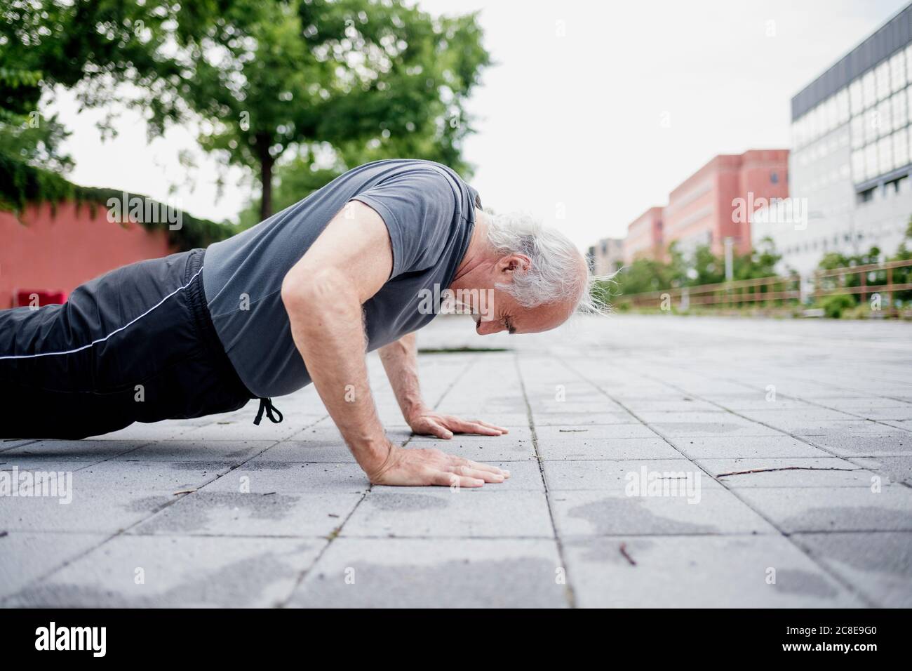 Active senior man doing push-ups on footpath in city Stock Photo