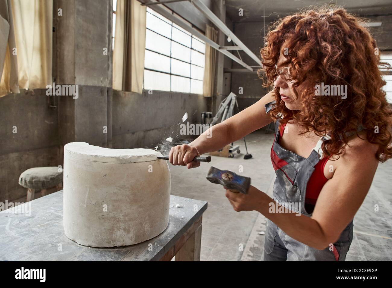 Female stonemason with curly hair carving stone on table in workshop Stock Photo