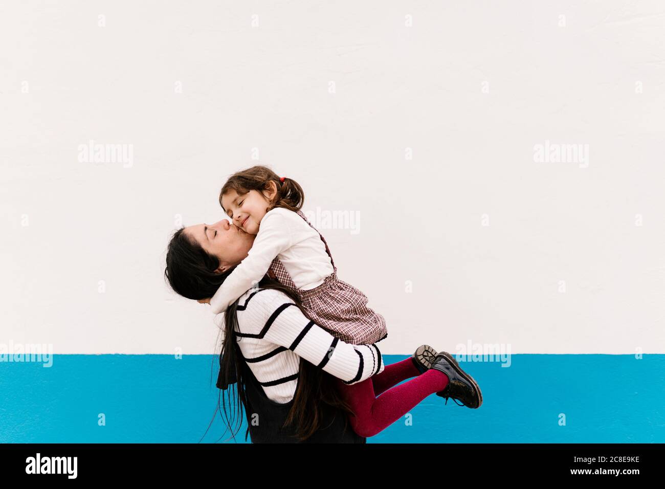 Mother kissing daughter on cheek against wall during sunny day Stock Photo