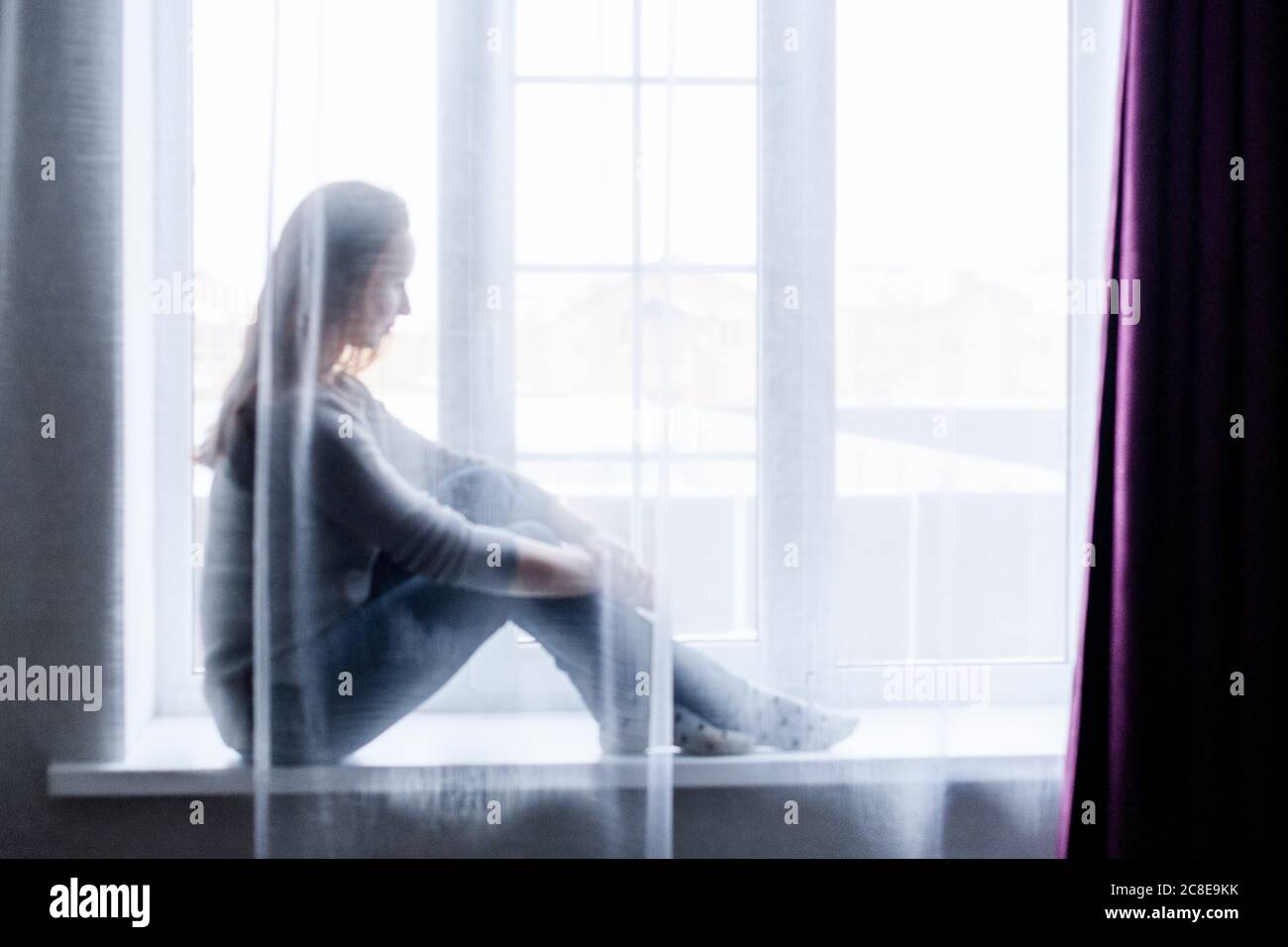 Young woman sitting on window at home Stock Photo