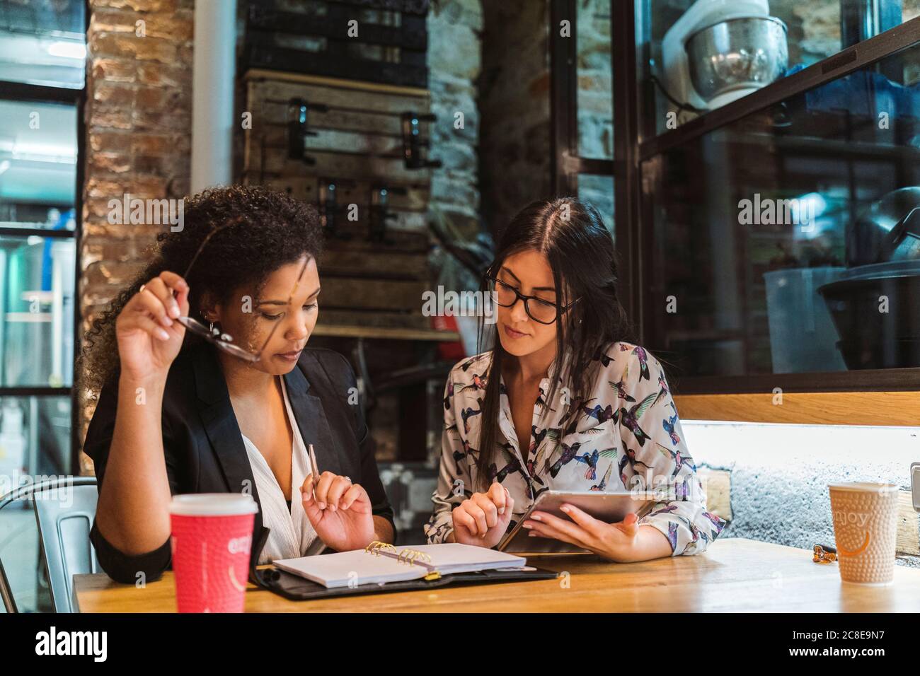 Multi-ethnic female colleagues discussing over digital tablet and diary while sitting at coffee shop during meeting Stock Photo