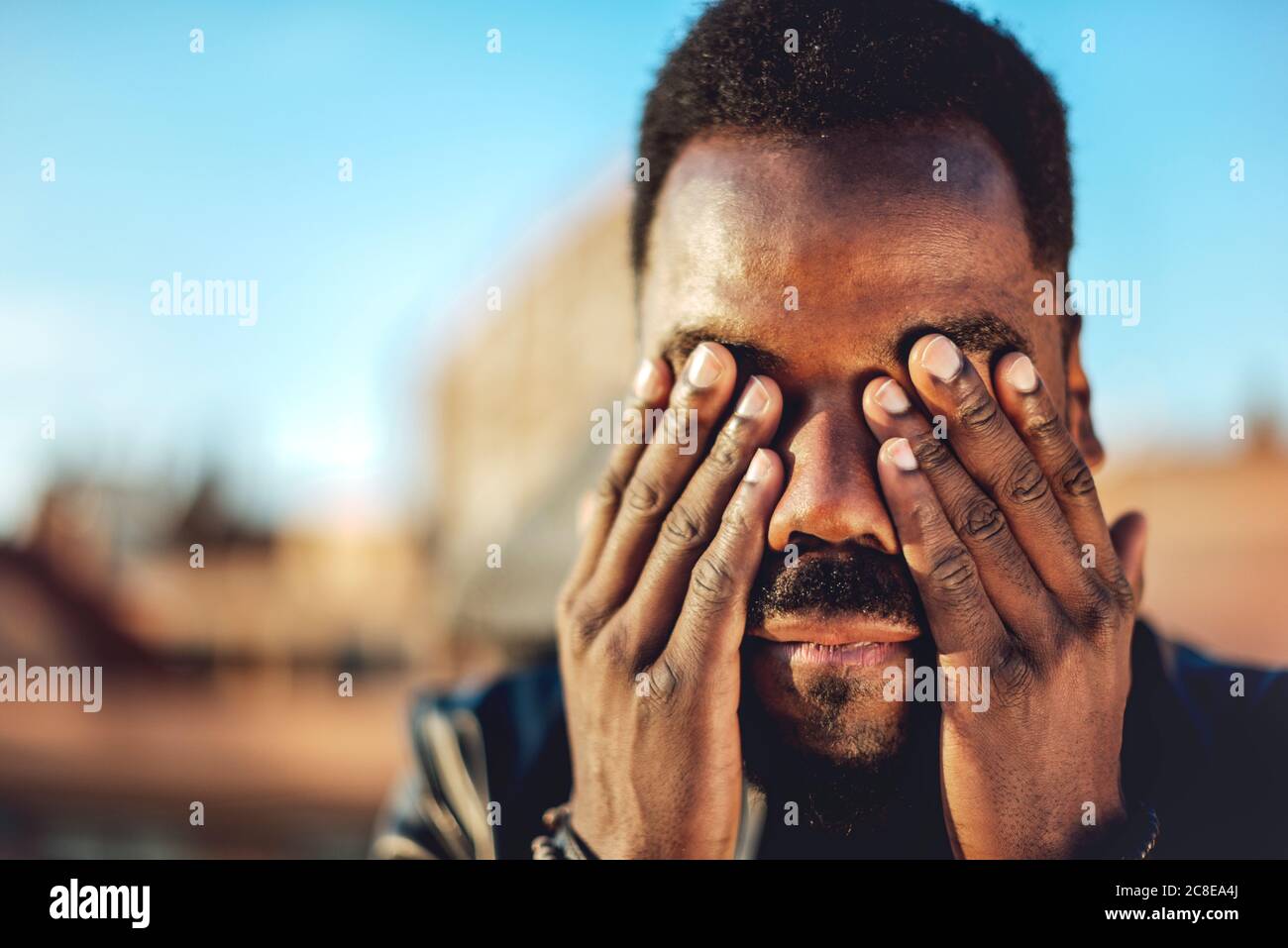 Close-up of young man with hands covering eyes on rooftop in city Stock Photo
