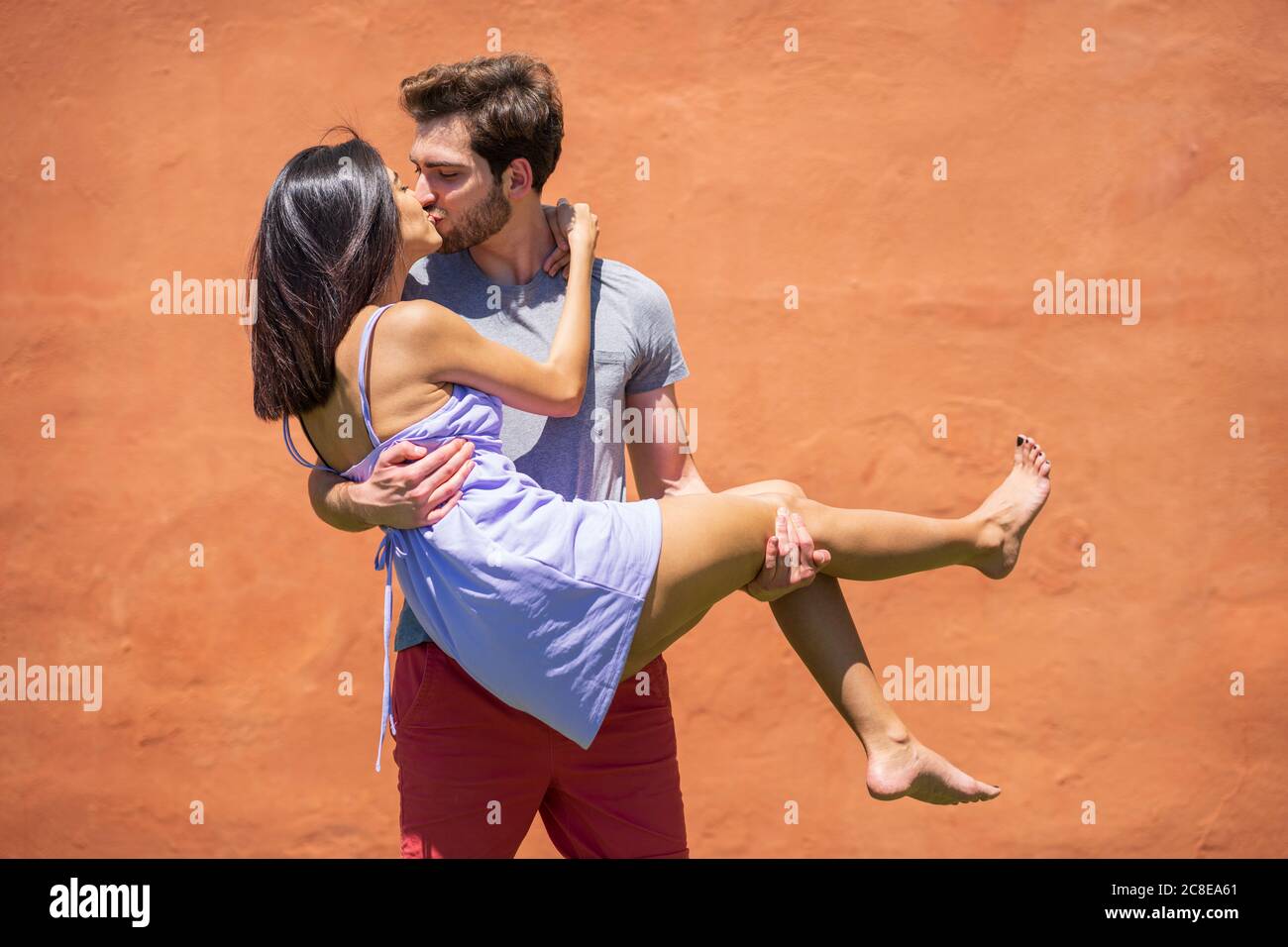Young man kissing while carrying woman against brown wall at back yard