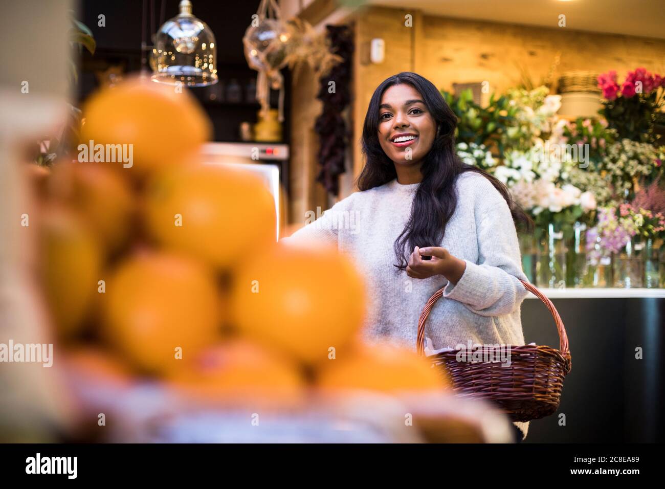 Happy young woman carrying wicker basket while shopping in grocery store Stock Photo