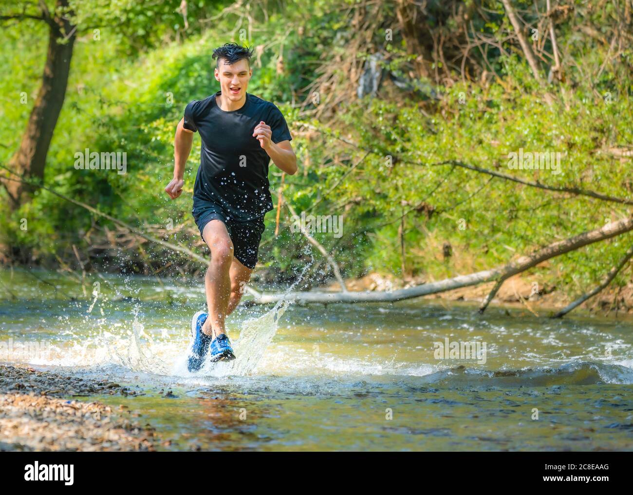 Young male athlete running while splashing water in stream Stock Photo