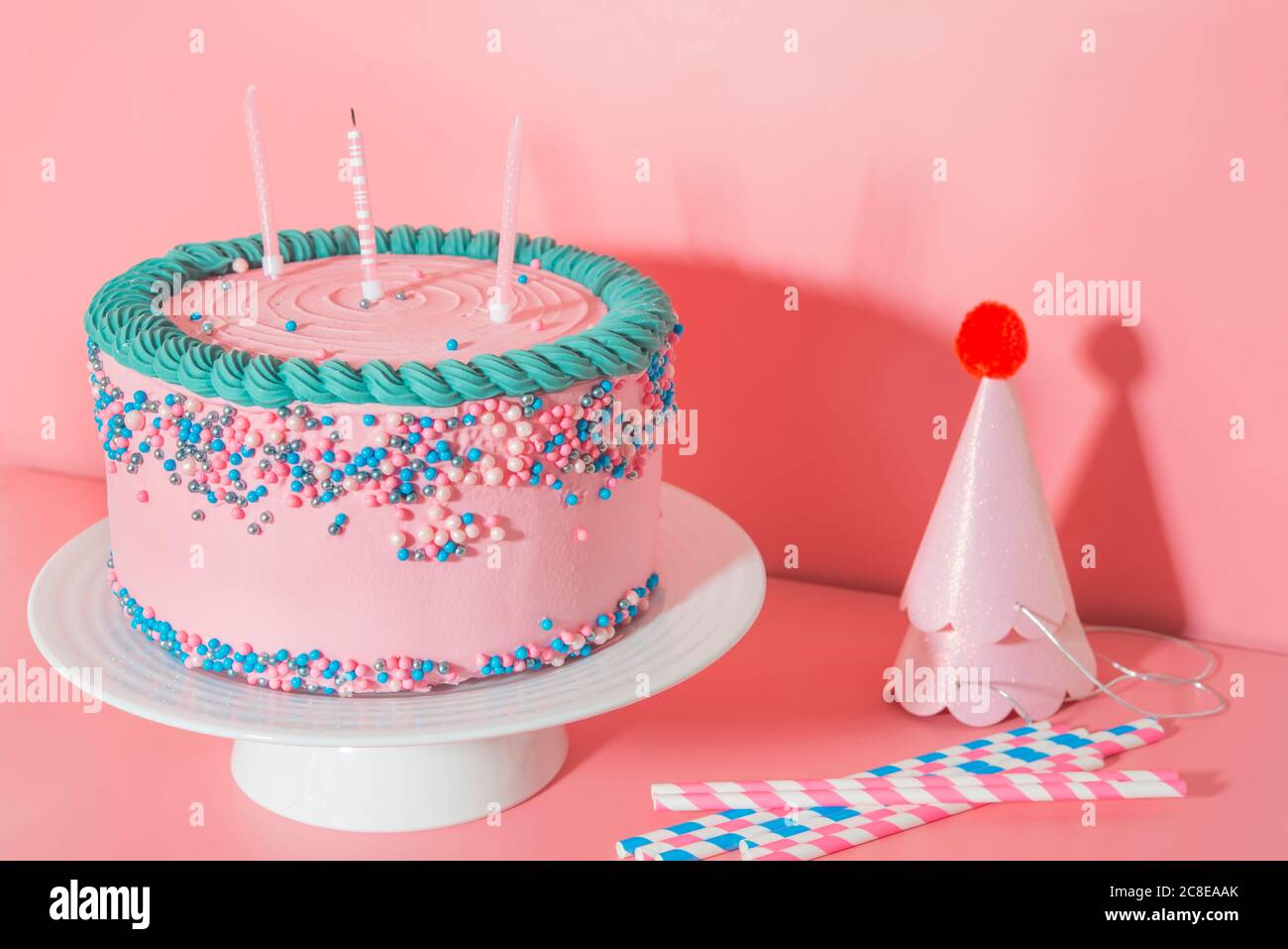 Cake stand with strawberry birthday cake, drinking straws and party hats Stock Photo
