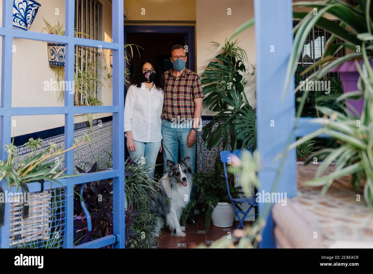 Couple wearing masks with dog standing at entrance of house seen