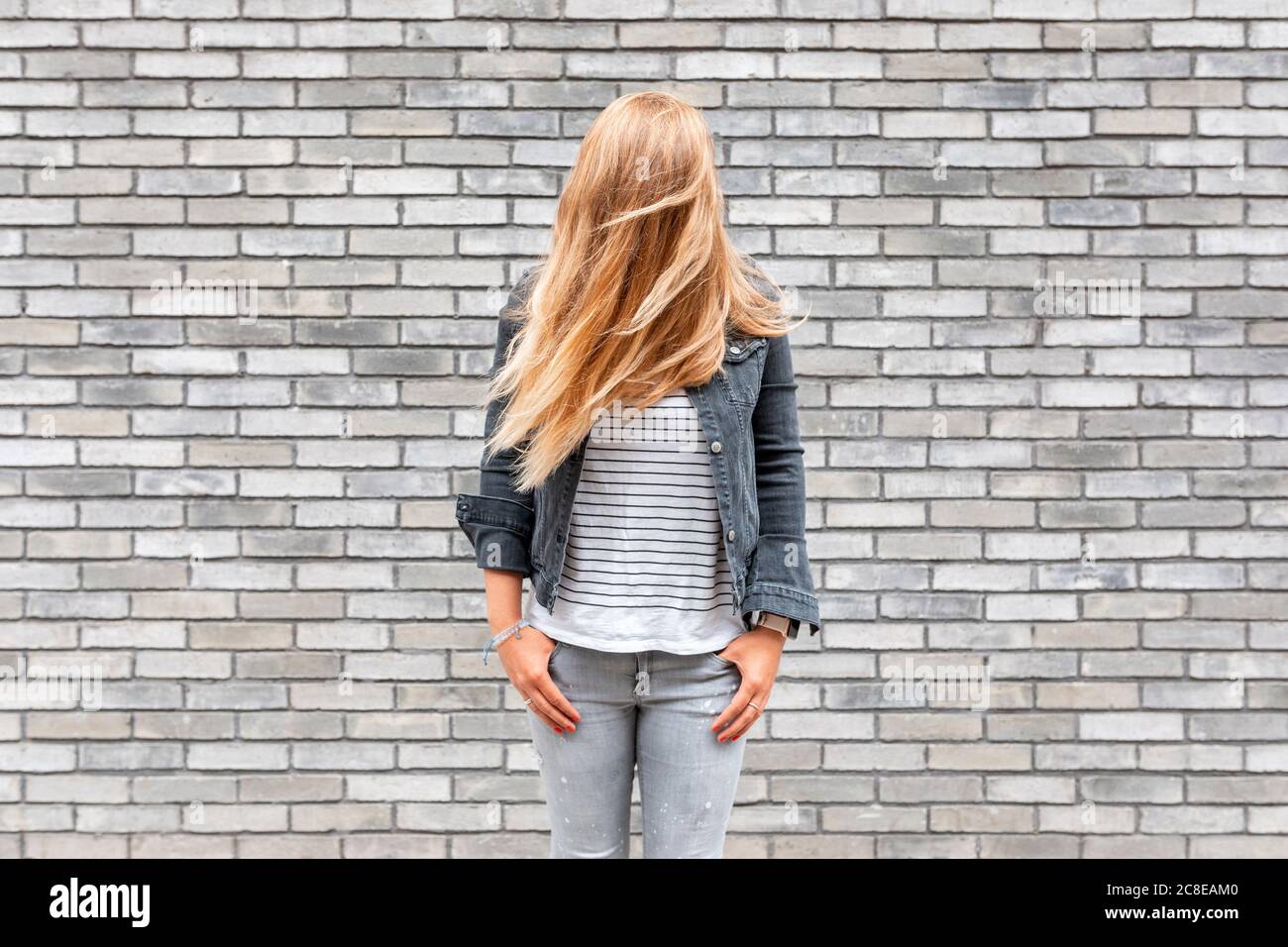 Woman with hair in front of face standing against gray brick wall Stock Photo