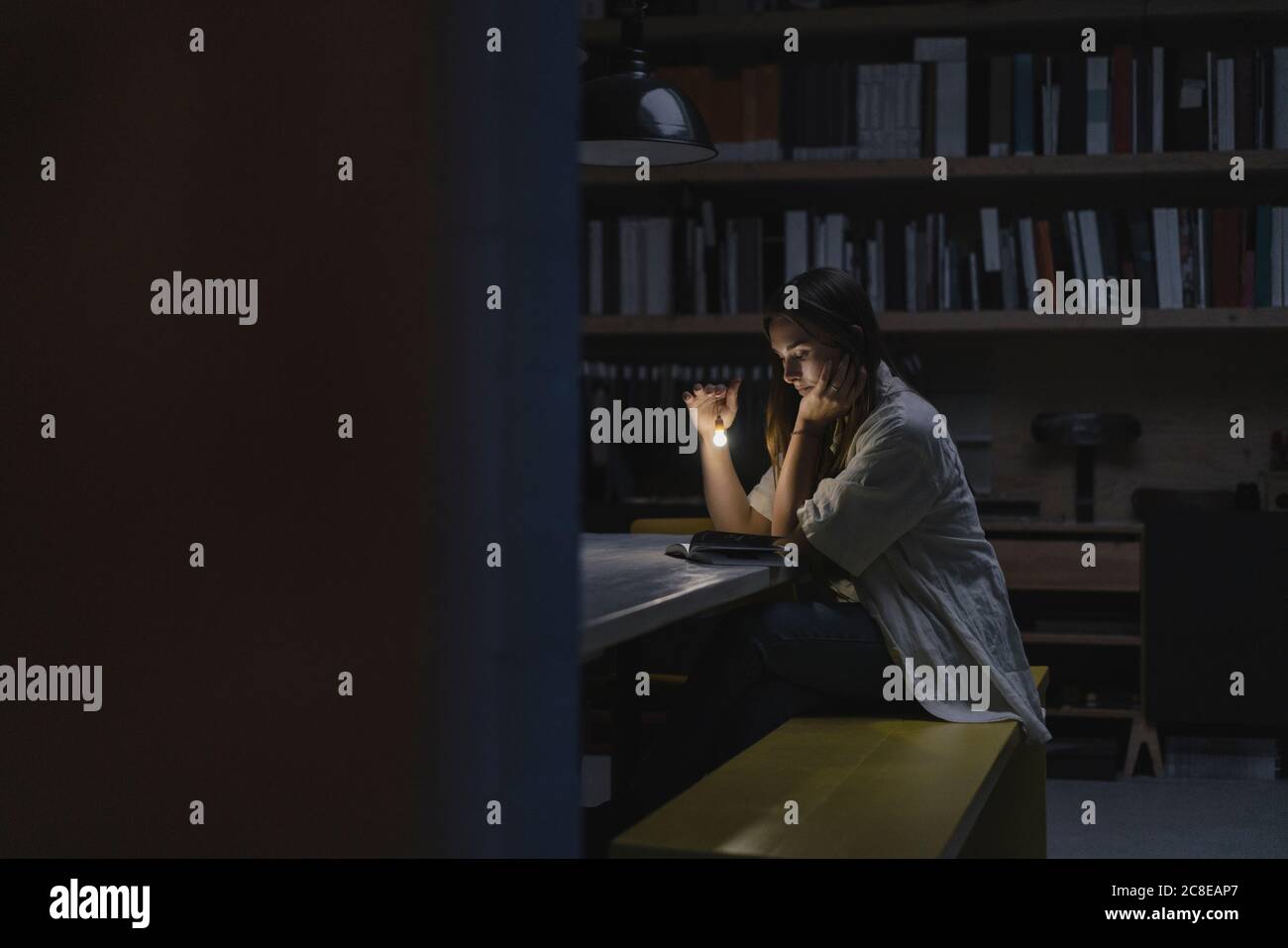 Young woman sitting in office, reading book at night with a torch Stock Photo
