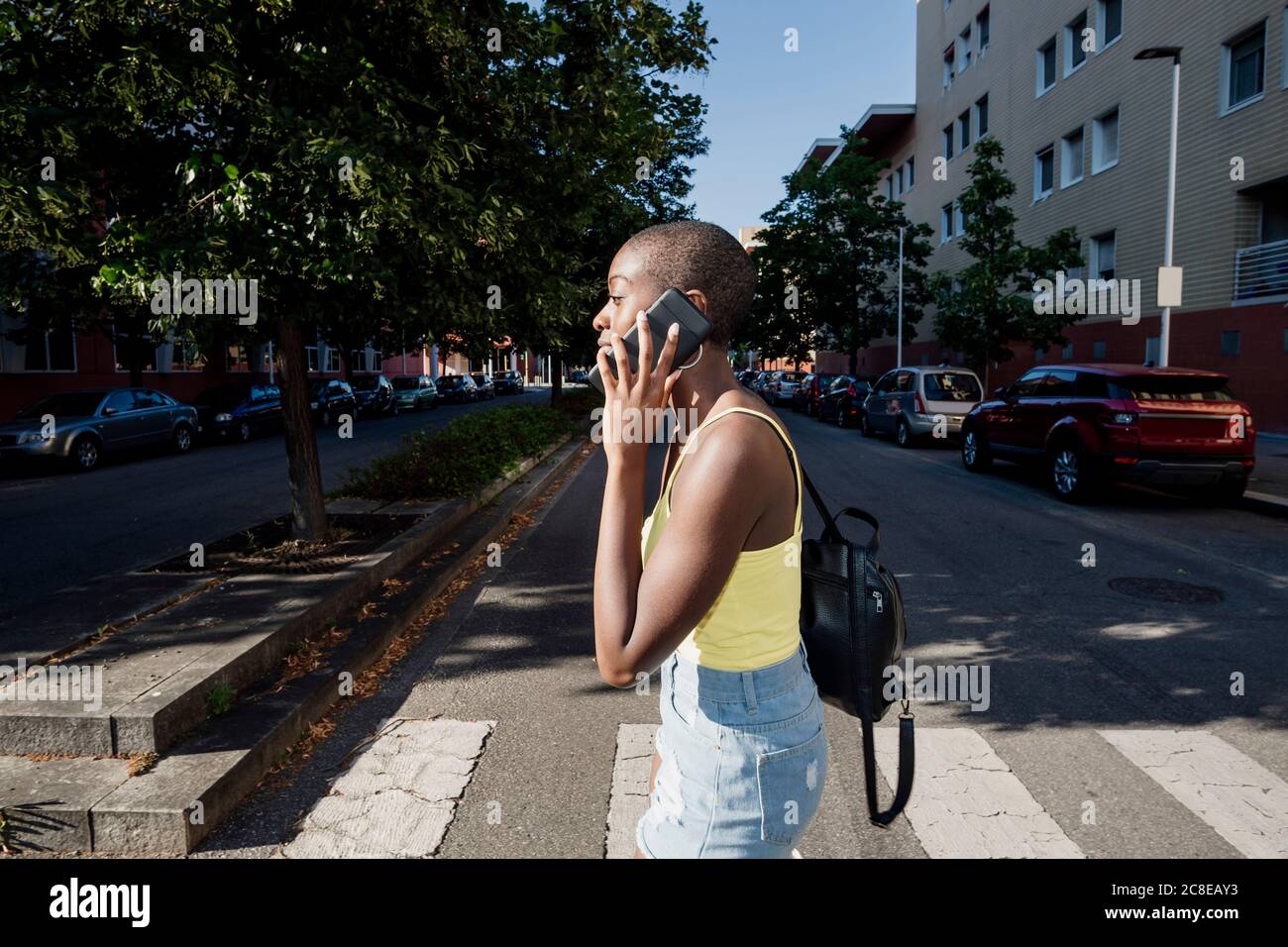 Young woman with shaved head talking over smart phone while walking on road in city Stock Photo