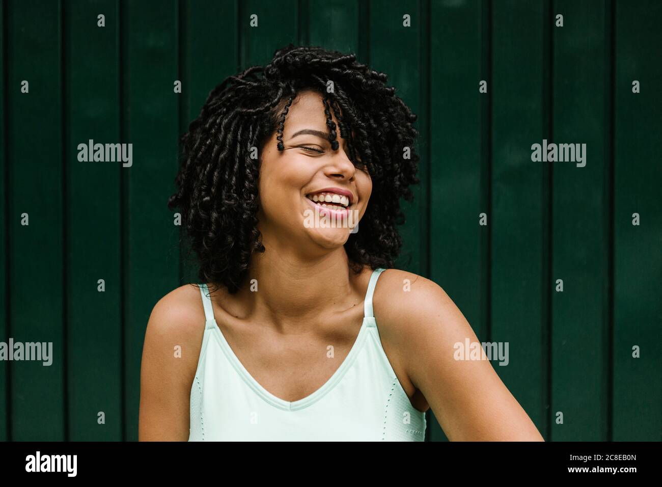 Cheerful young woman with eyes closed standing against metal door Stock Photo