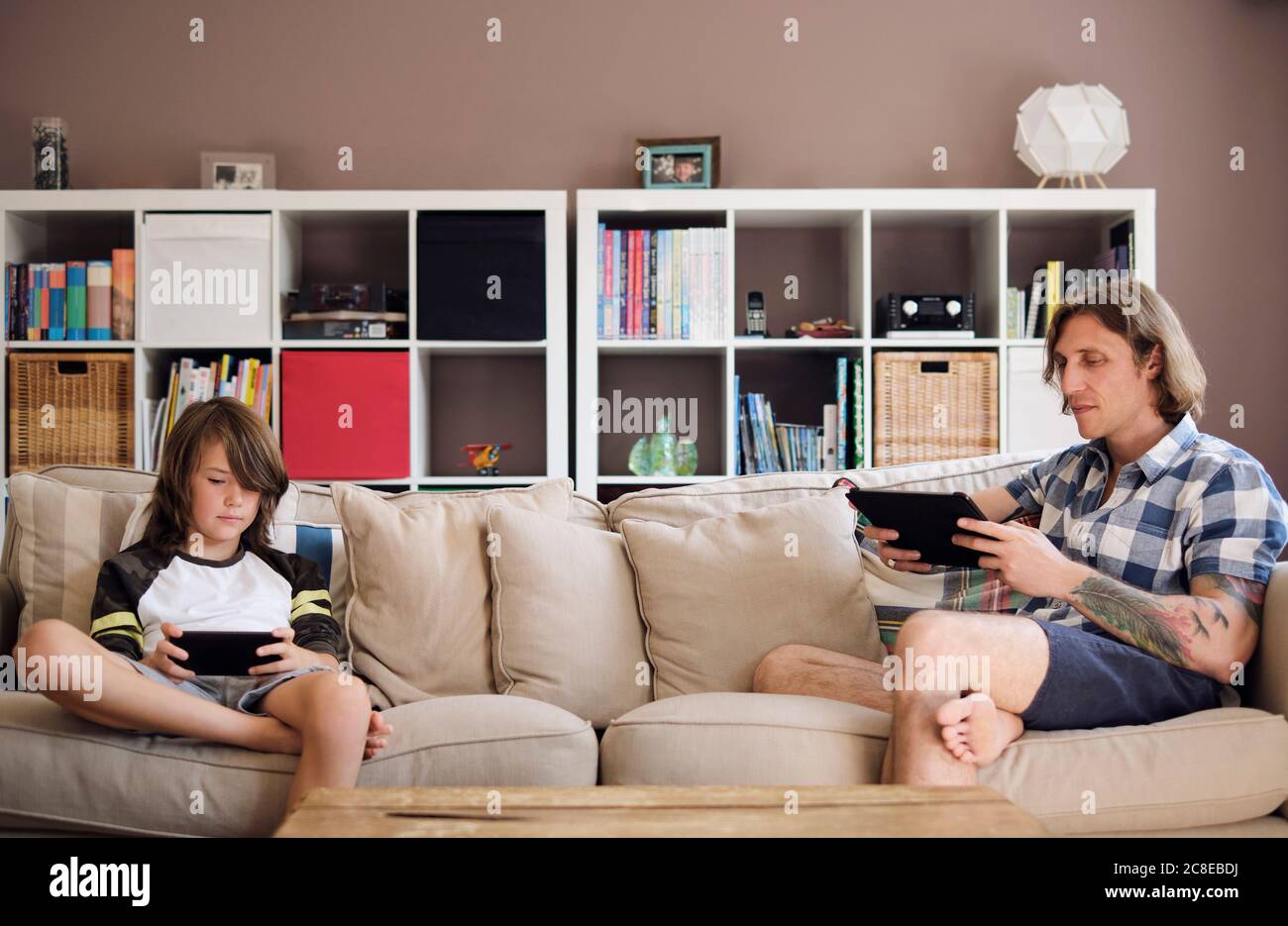 Father and son using technologies while sitting on sofa at home Stock Photo