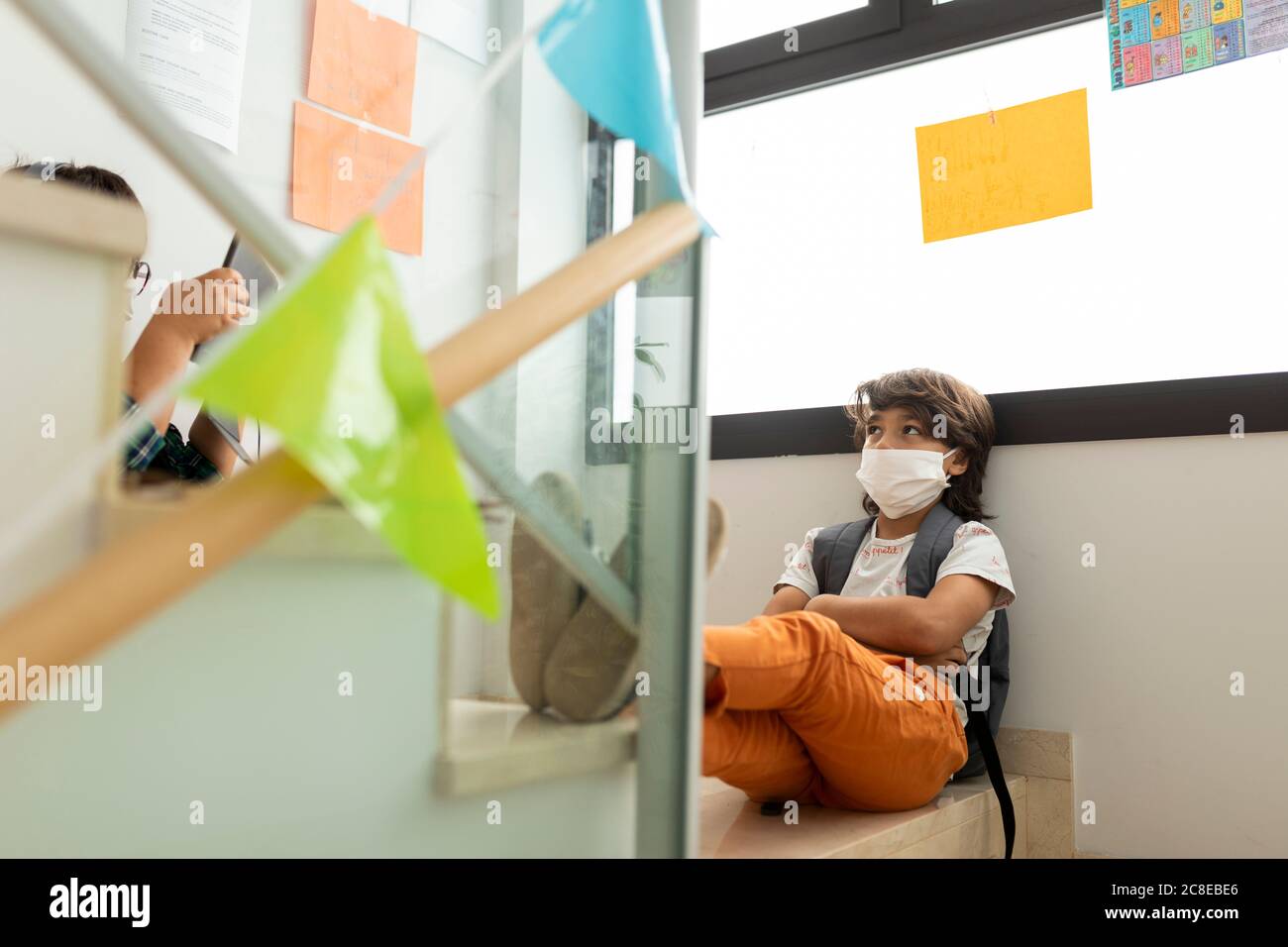 Boy wearing mask looking at friend using digital tablet while on steps in school Stock Photo