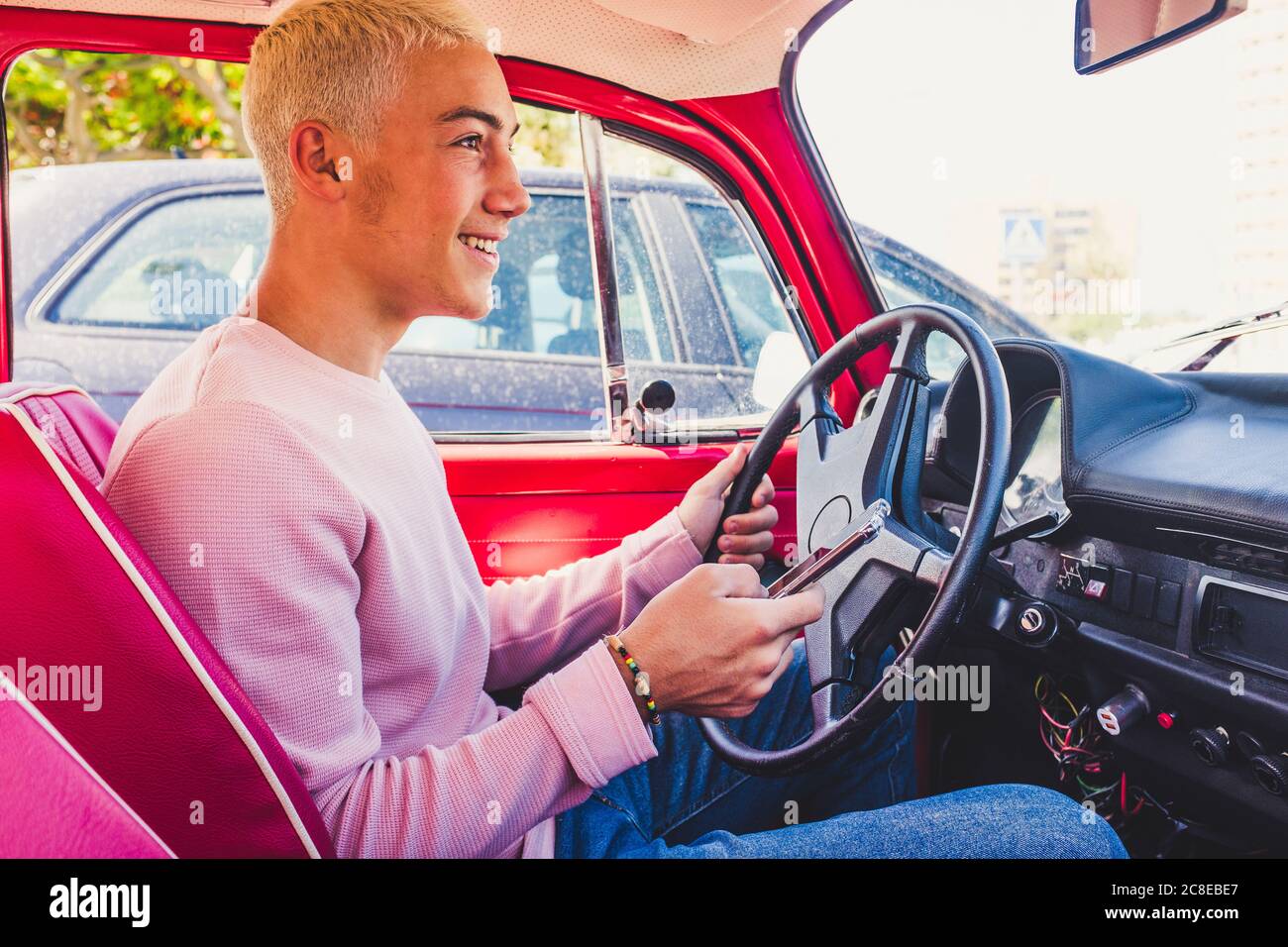 Smiling teenage boy sitting in vintage car with smartphone Stock Photo