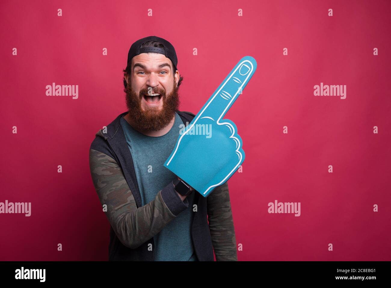 Happy man is pointing with a blue foam fan glove over red pink