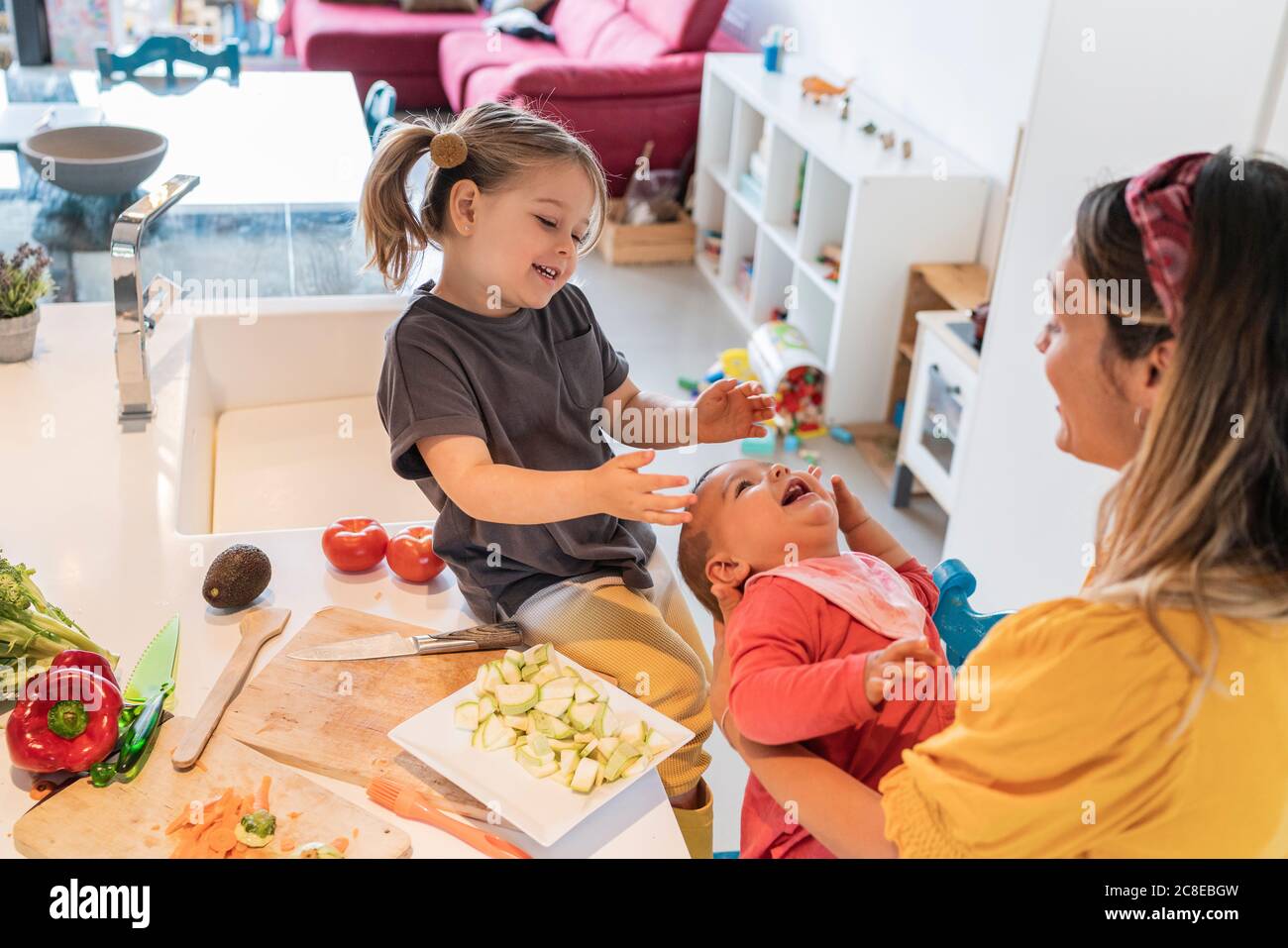 Happy mother and daughter playing with baby girl in kitchen at home Stock Photo