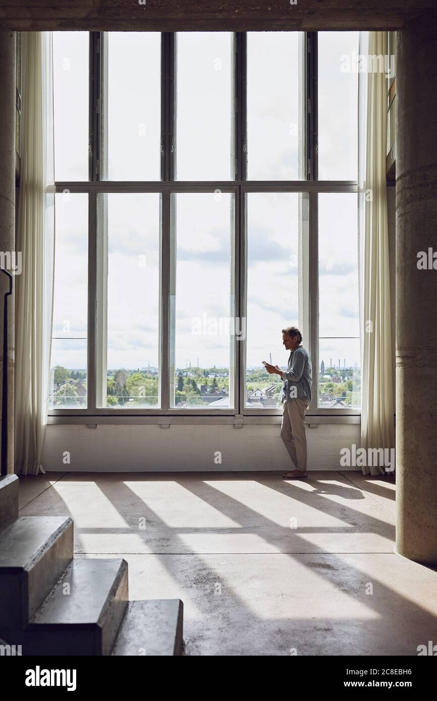 Senior man using smartphone at the window in a loft flat Stock Photo