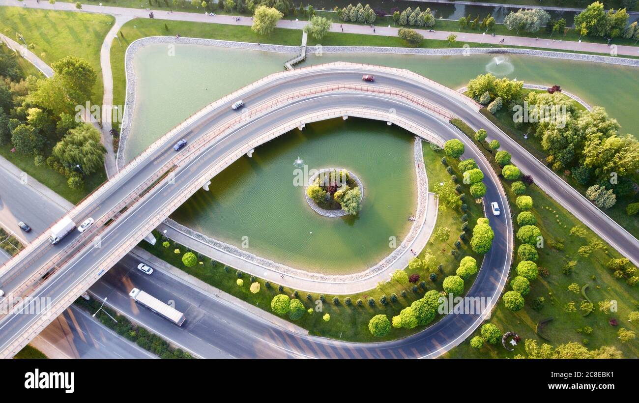 Aerial view of the roundabout on the river. Trees, overpass, buildings and vehicles can be seen. Stock Photo