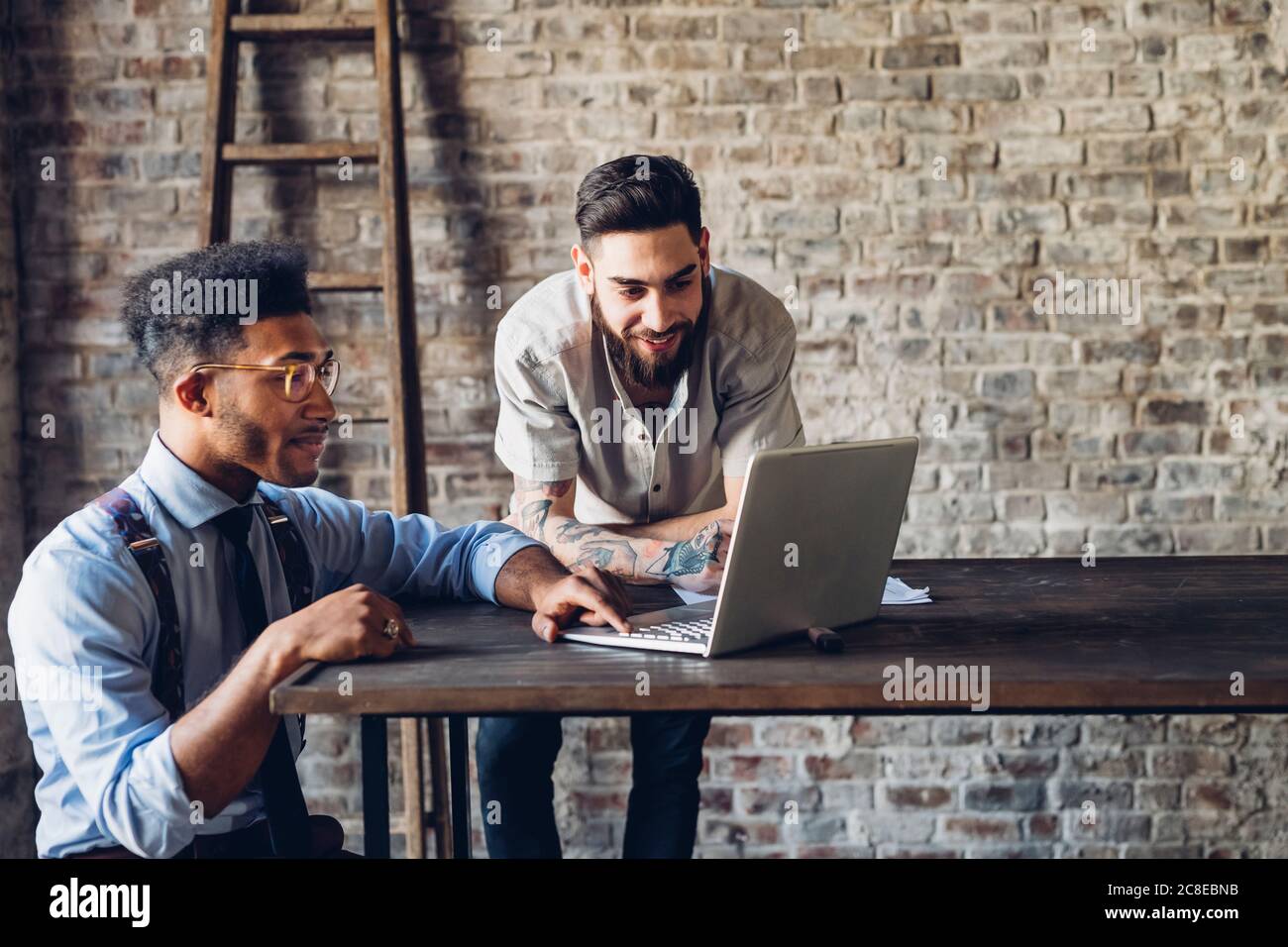 Two creative businessmen using laptop in loft office Stock Photo