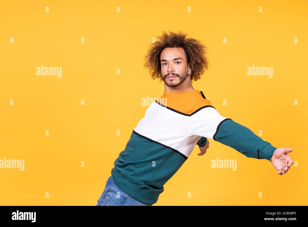 Cool young man with curly hair dancing against yellow background Stock Photo